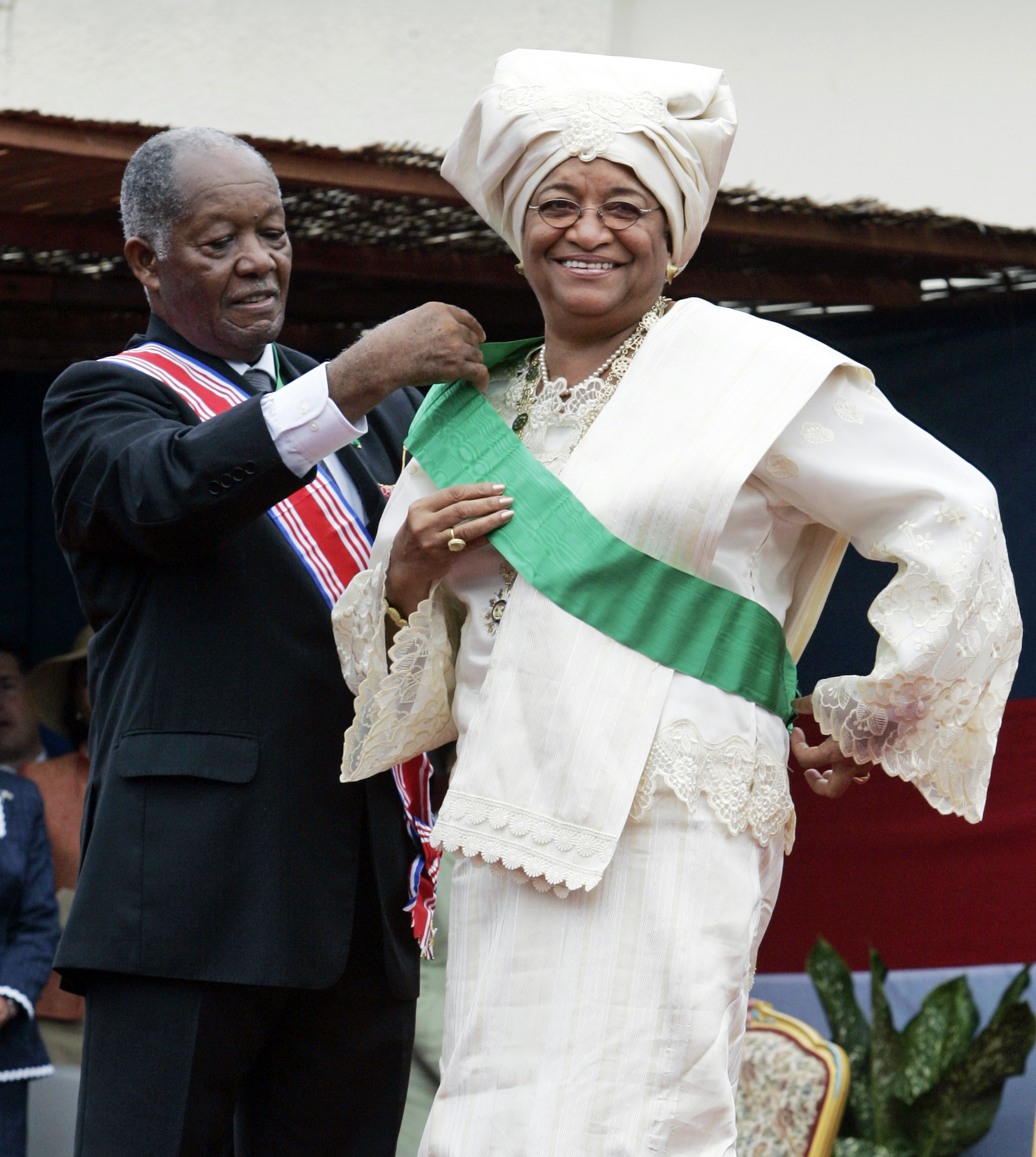 リベリアの新大統領、エレン-ジョンソン-サーリーフは、リベリアの上級大使ジョージ-W-ウォレス-ジュニアの支援を受けて大統領サッシ、モンロビア、リベリア、January16、2006のキャピトルビルでの彼女の就任式の間に。 サーリーフ大統領はアフリカで最初に選出された女性国家元首であった。 (AP Images/Charles Dharapak)'s Senior Ambassador-at-Large George W. Wallace, Jr., during her inauguration ceremony at the Capitol Building in Monrovia, Liberia, January 16, 2006. President Sirleaf was Africa's first elected female head of state. (AP Images/Charles Dharapak)