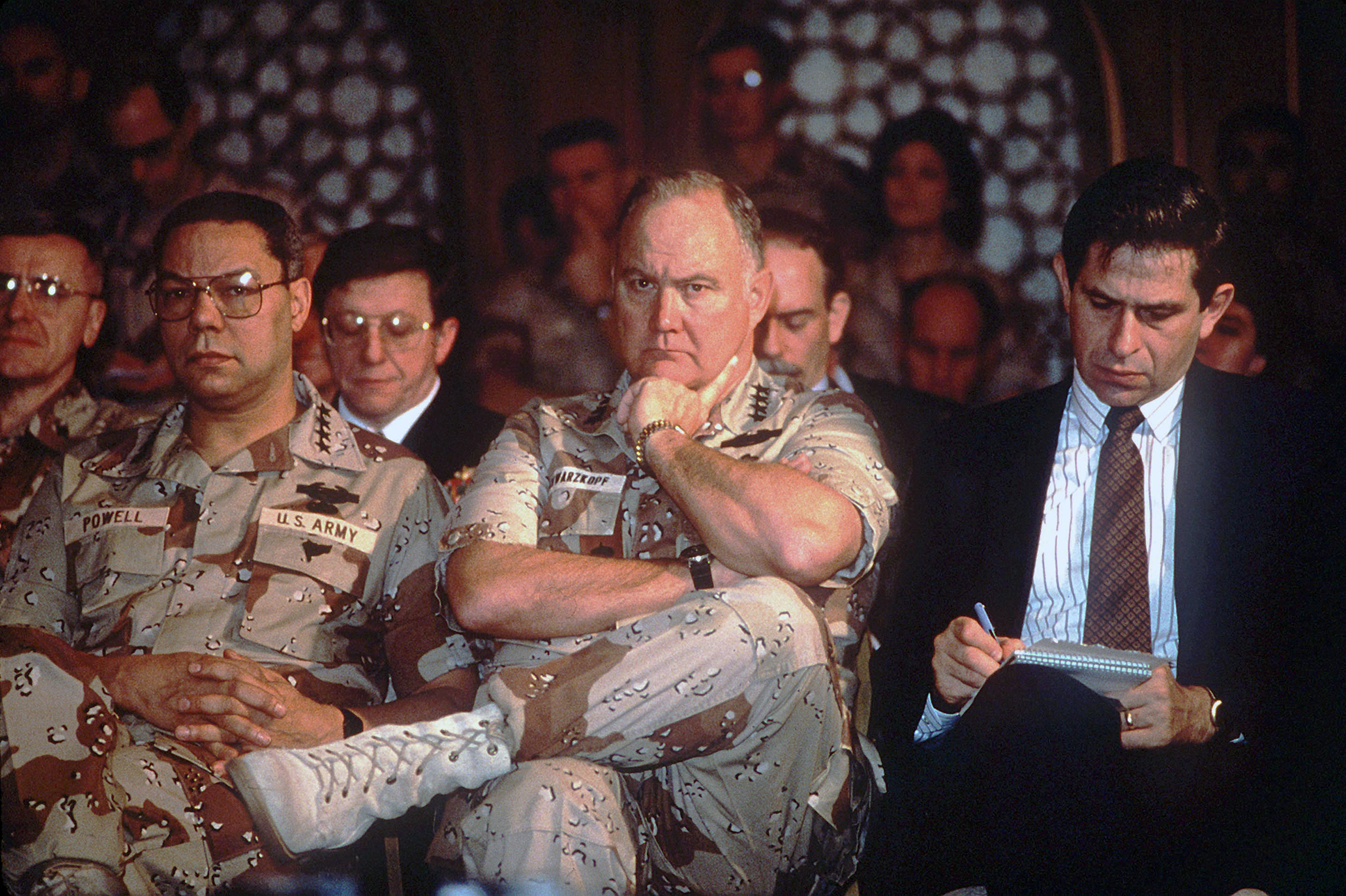 1991: Paul D. Wolfowitz, Under Secretary of Defense for Policy, right, takes notes while General Colin Powell, Chairman, Joint Chiefs of Staff, and General Norman Schwarzkopf, Commander-in-Chief, U.S. Central Command, listen to Secretary of Defense Richard Cheney answer questions from the media. The men are taking part in a press conference held by U.S. and Saudi Arabian officials during Operation Desert Storm.